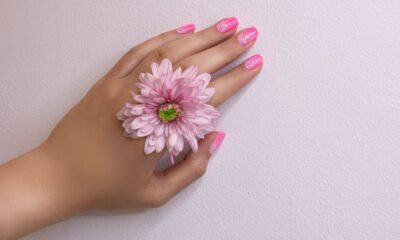 Close-up of a woman's hand with pink nails and a pink flower, showcasing delicate beauty.