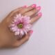 Close-up of a woman's hand with pink nails and a pink flower, showcasing delicate beauty.