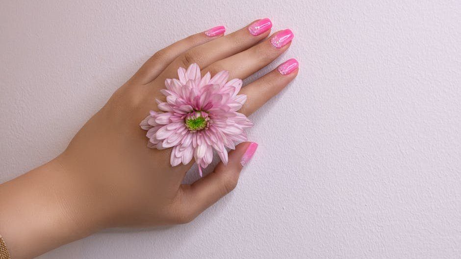 Close-up of a woman's hand with pink nails and a pink flower, showcasing delicate beauty.