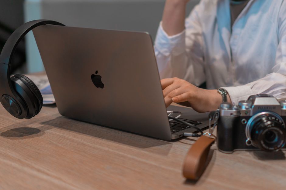 Doi studenți discută la o masă de cafenea, cu un laptop deschis și cu caiete în față