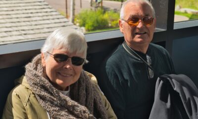 Doi oameni pe canapea, cu un laptop deschis, lângă o fereastră cu stropi de ploaie