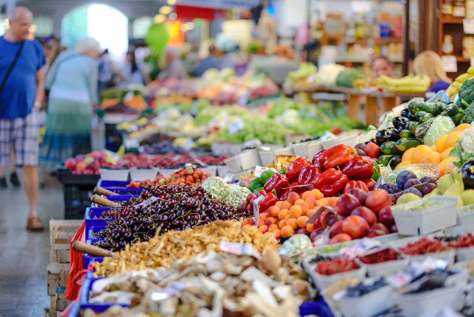 Două femei aleg legume proaspete la un stand de piață într-o dimineață însorită
