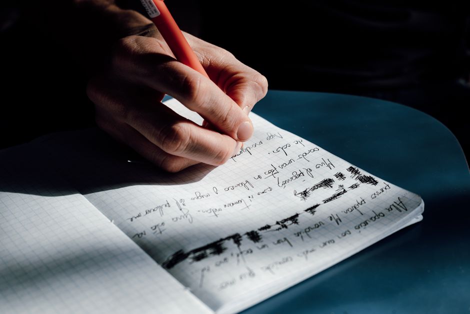 Bărbat concentrat, cu un carnet deschis pe birou, seara, notând idei
