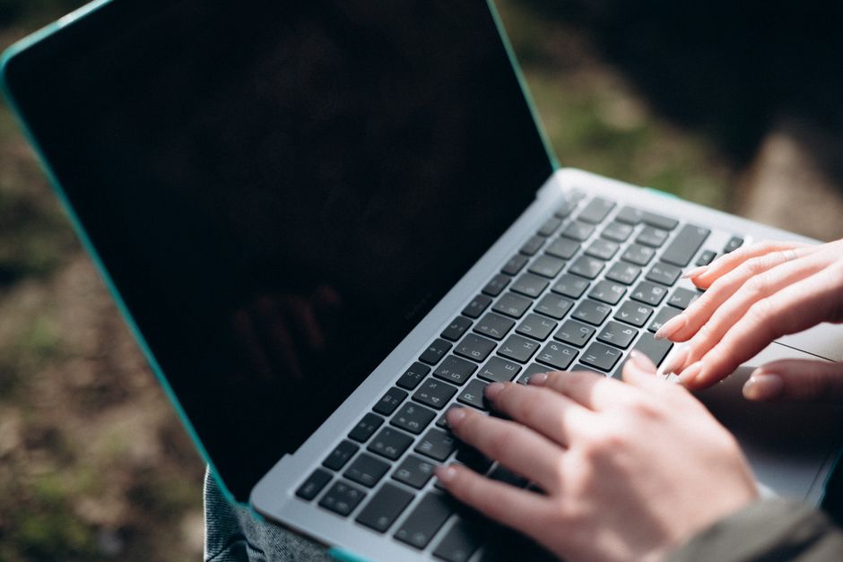 Trei studenți așezați la o masă de bibliotecă, cu laptopuri și caiete deschise