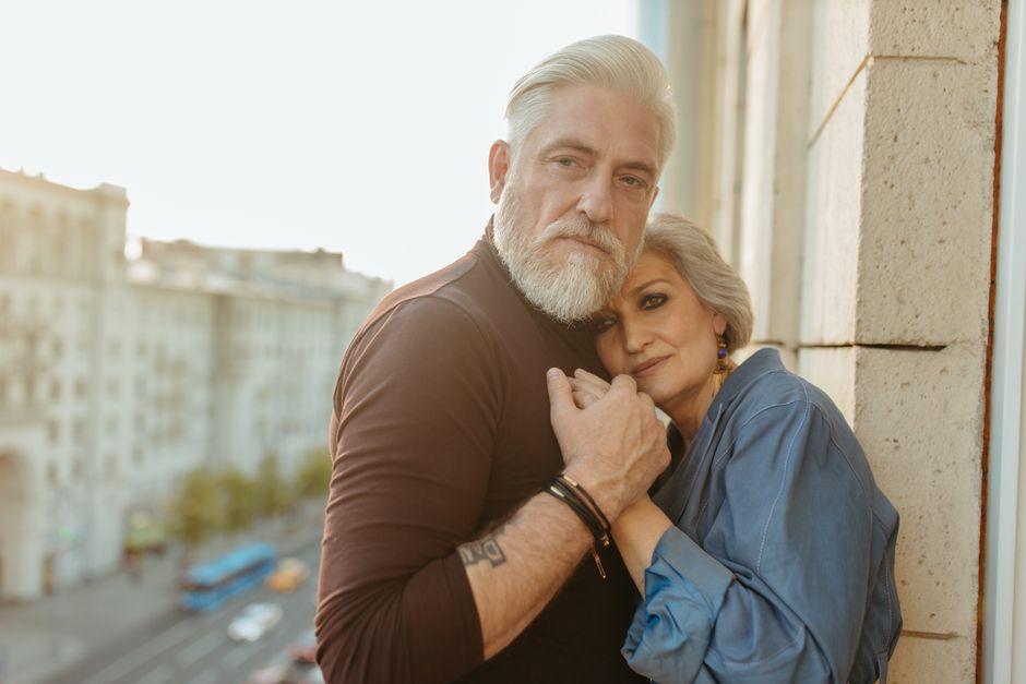 Un bărbat în vârstă la masă, cu laptopul deschis, discutând cu familia