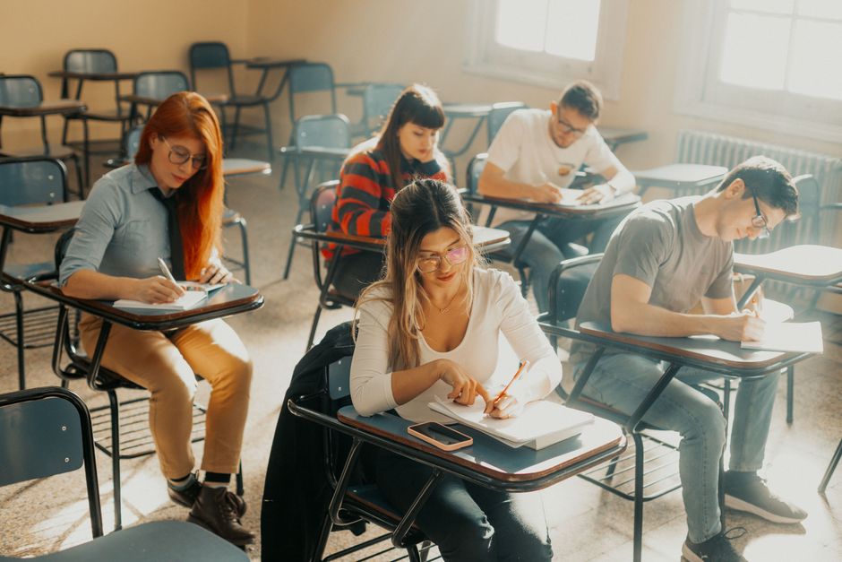 Student la o masă de lângă geam, seara, cu un caiet deschis și o lampă aprinsă