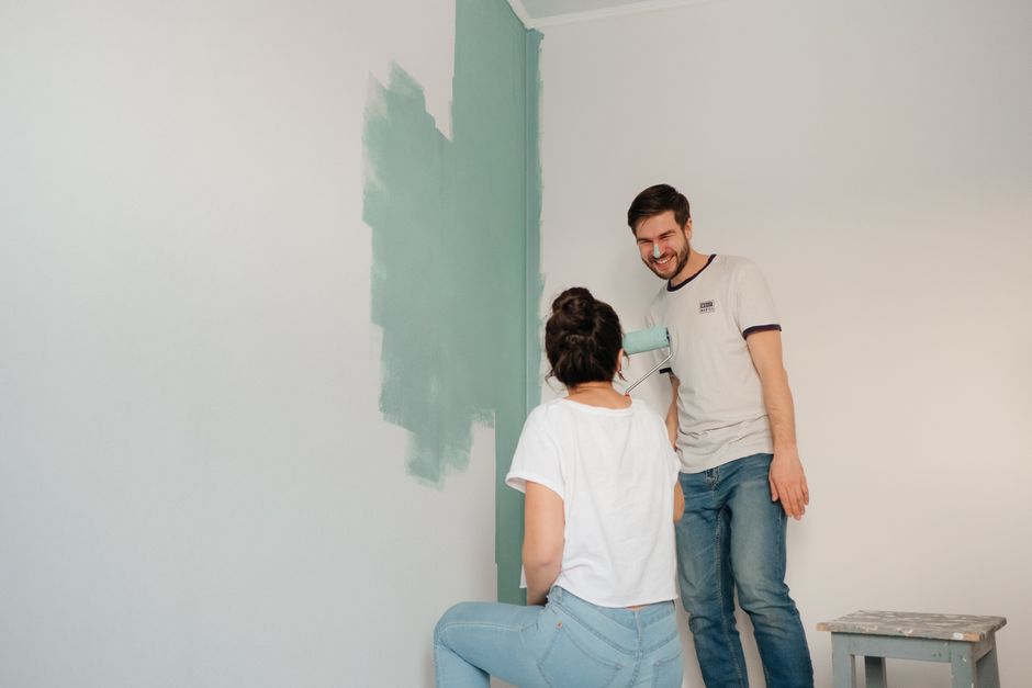 Tânără cu rolă și găleată de vopsea într-un apartament aproape gol